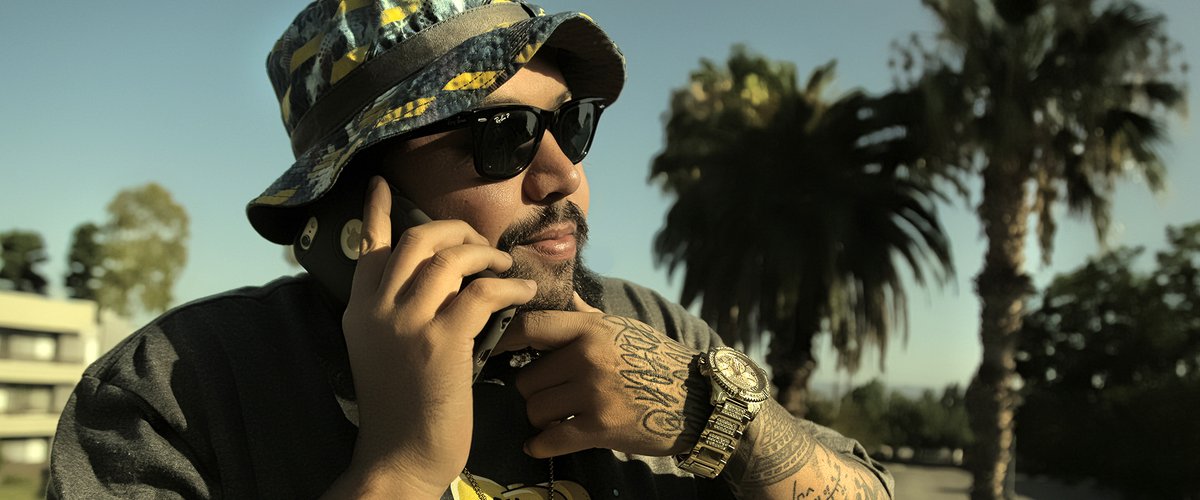 DJ Pumba, Snow Tha Product's main producer and tour DJ, wearing sunglasses and a bucket hat in front of palm trees in Los Angeles